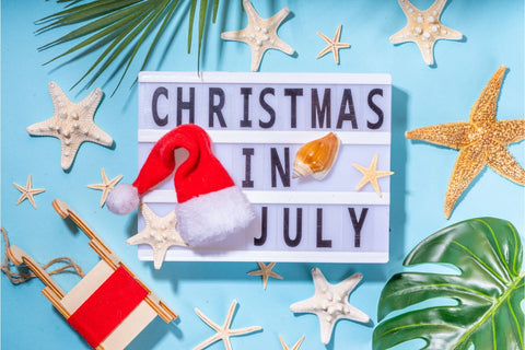 Sign with "Christmas in July" message, a Santa hat, and beach decorations.