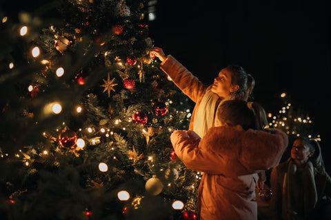 Family decorating a Christmas tree at night outdoors.
