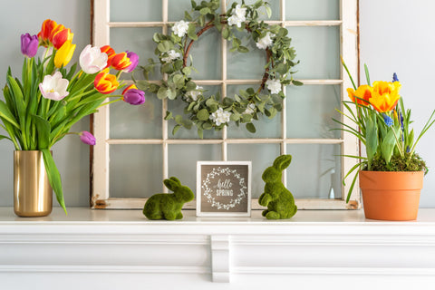 Mantel decorated with Easter decorations, artificial green bunnies, flowers, and artificial wreath.