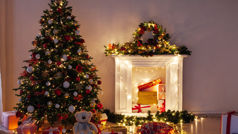 A traditional Christmas tree next to a fireplace, decorated with red and gold ornaments and stockings hanging above.