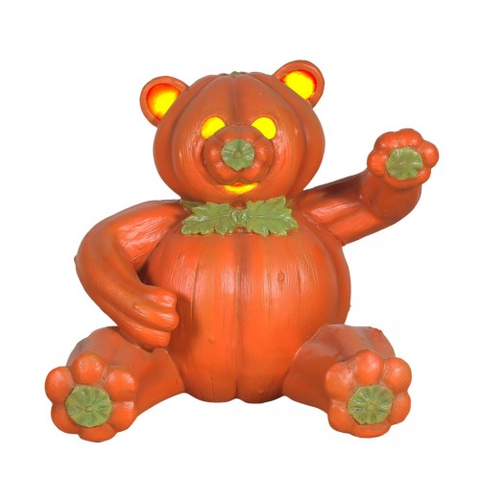 A bear sculpture made to look like a pumpkin, with glowing eyes, a green nose, and paw pads. The bear is sitting and raising one arm.