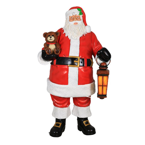 A statue of Santa Claus holding a teddy bear in one hand and a lantern in the other, dressed in traditional red and white attire.