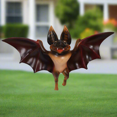 Smiling statue bat with outstretched wings, hovering outside.